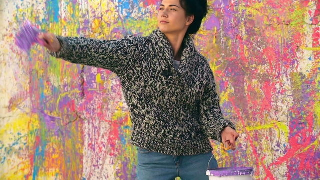 Beautiful female painter splashing colorful paint on walls in slow motion