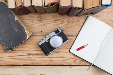 Top view on wooden desktop with books, notepad and camera