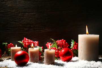 Burning candles and Christmas accessories with snow on wooden background