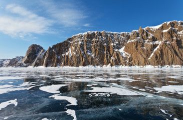 Beautiful winter landscape with smooth ice near rocky shore of frozen Lake Baikal