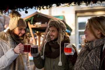 Couple and friend, Friends on a german  Christmas market enjoying traditional mullet wine and talk to each other - obrazy, fototapety, plakaty