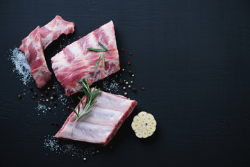 Raw fresh pork ribs over black wooden background, above view