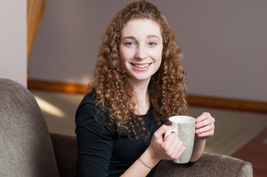 young curly haired caucasian woman sitting down enjoying a cup of tea