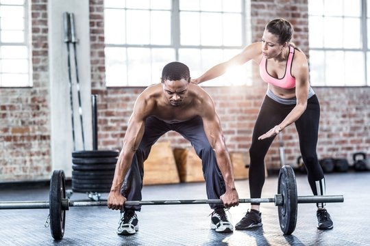 Female trainer helping fit man lifting barbell