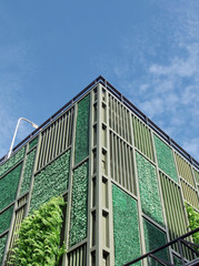 Corner of building with gray ventilation grille, plants and artificial turf on its facade