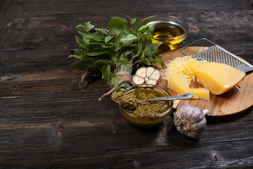 Green basil pesto - italian recipe ingredients on black chalkboard background from above. Parmesan cheese, basil leaves, pine nuts, olive oil, garlic. Layout with free text space.