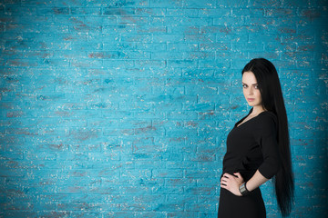 Beautiful young woman in a black dress posing against the backdrop of a blue brick wall