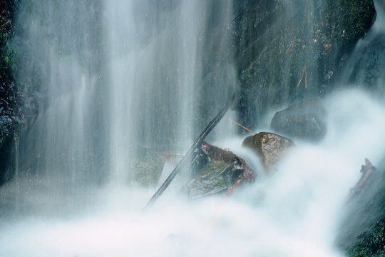 Water Spray Below Small Waterfall On Mountain Stream, Water Is Falling Over Mossy Boulder. The Spray Create On Level And Gravel Milky Water. Broken Branches In Water