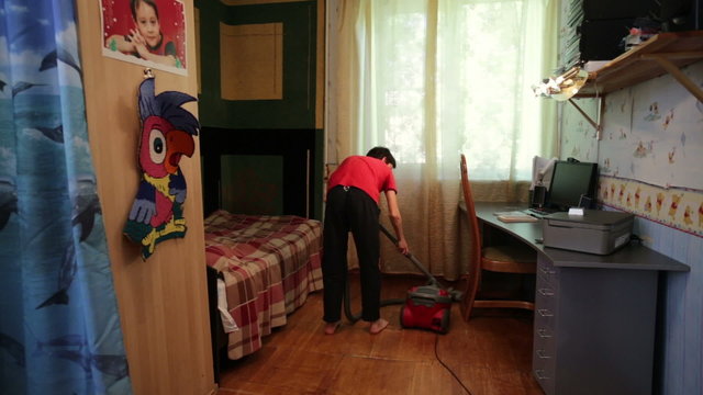 Teen boy vacuuming the floor in the room