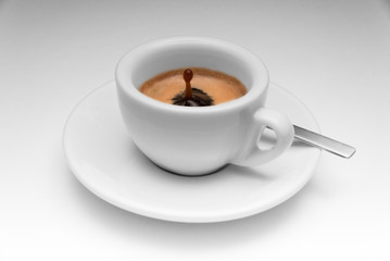 Espresso in einer schlichten weißen Tasse, auf dem Unterteller ein Löffel. Perfekter Tropfen aus dem Kaffee heraus.