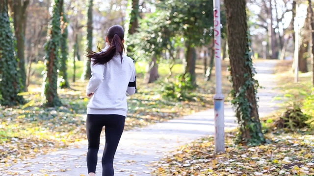Sporty young woman running in the park and listening to music. Sport lifestyle. Slow motion.