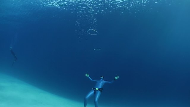 Lady freediver makes ring bubbles underwater on the depth