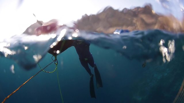Free divers relaxing near the buoy, preparing for the dive. Split footage with underwater view and sky in the frame. Focus underwater only