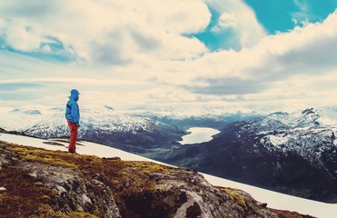 Obraz premium Vintage landscape of a tourist stands on a hilltop and look at the lake in the valley. Blue sky with clouds. Snowy mountains. Norway.