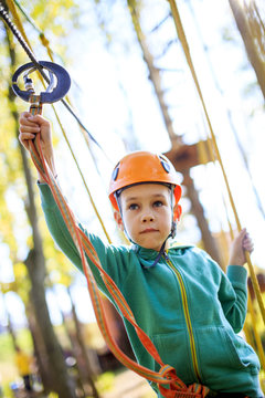 boy overcomes the obstacle course in rope park. Boy biting her lip on a complex rope climbing structure