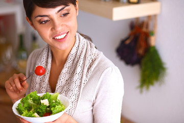 Young woman eating fresh salad in modern kitchen