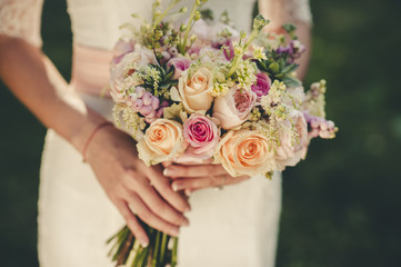 Portrait of a wedding bride posing in a white hipster style dress with flowers in her hands in the forest on sunset