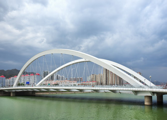 Fototapeta na wymiar White bridge over a green canal with dramatic clouds, Zhangjiakou, China