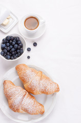 Couple of croissants on a white plate with coffee and blueberries. selective focus. top view.