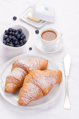 Couple of croissants on a white plate with coffee and blueberries. selective focus.