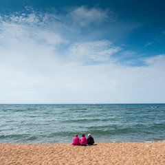 Young girls sitting on the shore of the lake Baikal in the summer, when it's windy.