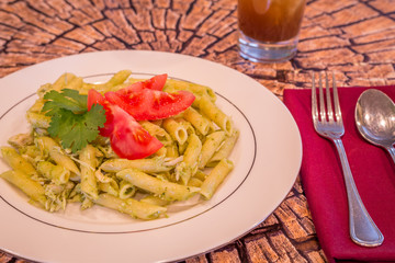 Pesto penne pasta with fresh tomatoes and iced tea on a tree stump background.