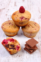 Fresh baked muffins with raspberries and chocolate on wooden background, delicious dessert