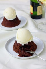Two molten chocolate cakes with ice cream on white linen, with glass of champagne in the background. Selective focus.