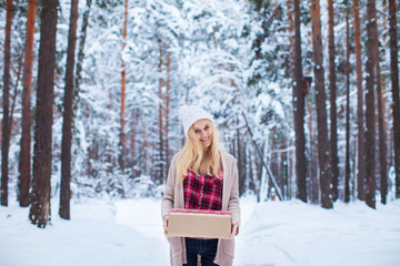 blonde girl holding a Christmas gift in winter forest