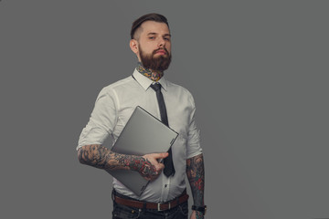 Bearded tattoed man in white shirt holding laptop.