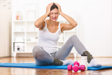 Young girl sitting on a floor mat after exercise, feeling pain.