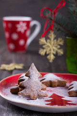 Homemade Christmas cookies in the shape of a Christmas tree, sprinkled with powdered sugar on a dark wooden table with festive decorations, selective focus