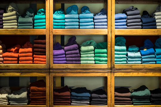 Various color sweatshirts at shelf and shirts on hangers in shop, Italy