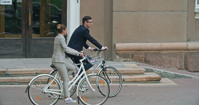 Tracking shot of elegant business couple biking down the street and talking 