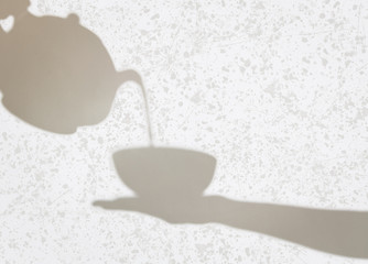 Delicate shadows of teapot pouring liquid into a cup held by fem