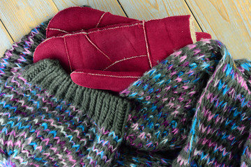 Fototapeta na wymiar close up of knitted hat, scarf and mittens gloves in grey ,bordeaux wine red blue and purple colors on a wooden shelves planks table with a empty room copy space 
