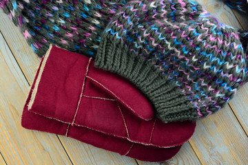 close up of knitted hat, scarf and mittens gloves in grey ,bordeaux wine red blue and purple colors on a wooden shelves planks table with a empty room copy space
