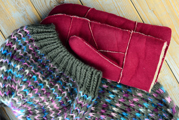close up of knitted hat, scarf and mittens gloves in grey ,bordeaux wine red blue and purple colors on a wooden shelves planks table with a empty room copy space
