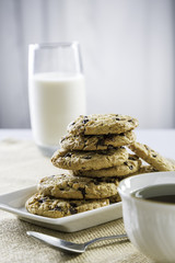 cookies stacked on each other on plate, glass of milk and cup of tea/coffee