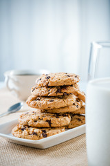 cookies stacked on each other on plate, glass of milk and cup of tea/coffee
