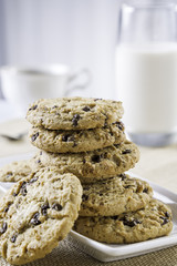 close up of cookies stacked on each other on plate, glass of milk and cup of tea/coffee