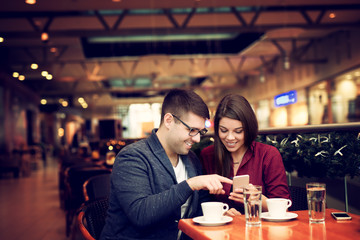 Lovely young couple looking at smart phone at cafe in trade center. Copy space for your text. Shallow depth of field. Very useful photo for processing with one click on edit image.