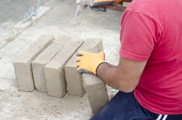 Bricklayer working with mud bricks for building a wall.