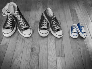 A photo of two pairs of adults shoes in black and white next to a pair of baby shoes in blue
