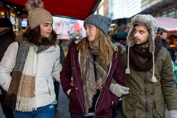 Couple and Friend walk over the Christmas Market and talk to each other and watch the Stands