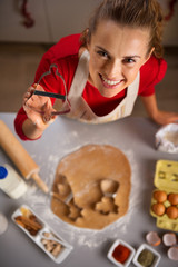 Young housewife showing Christmas cookie cutter while in kitchen