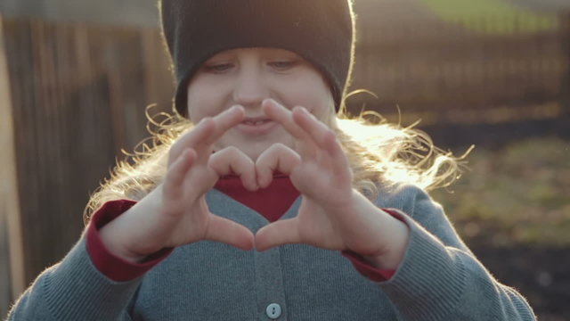 Wonderful girl folded her hands in a heart shape on a bright sunny day