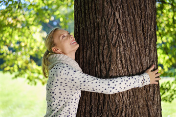 lächelnde frau umarmt einen baum und schaut nach oben