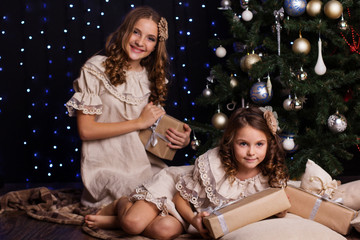 Two sisters with gifts near christmas tree