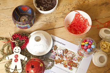 Decorating Gingerbread. A wooden table has the ingedients and recipe for gingerbread men sitting on it along with two tealights and Christmas decorations.